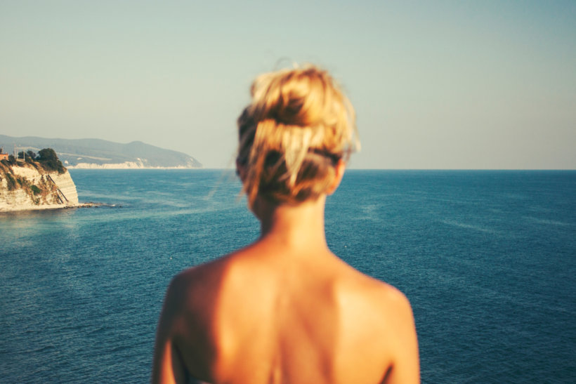 topless woman standing facing blue sea under white sky