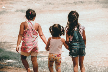 three girls holding each other hand walking towards brown soil