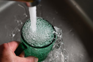 a person's hand is holding a green cup with water coming out of it