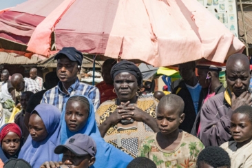 A woman, men, girls and boys with sad faces looking straight outside in an open area market